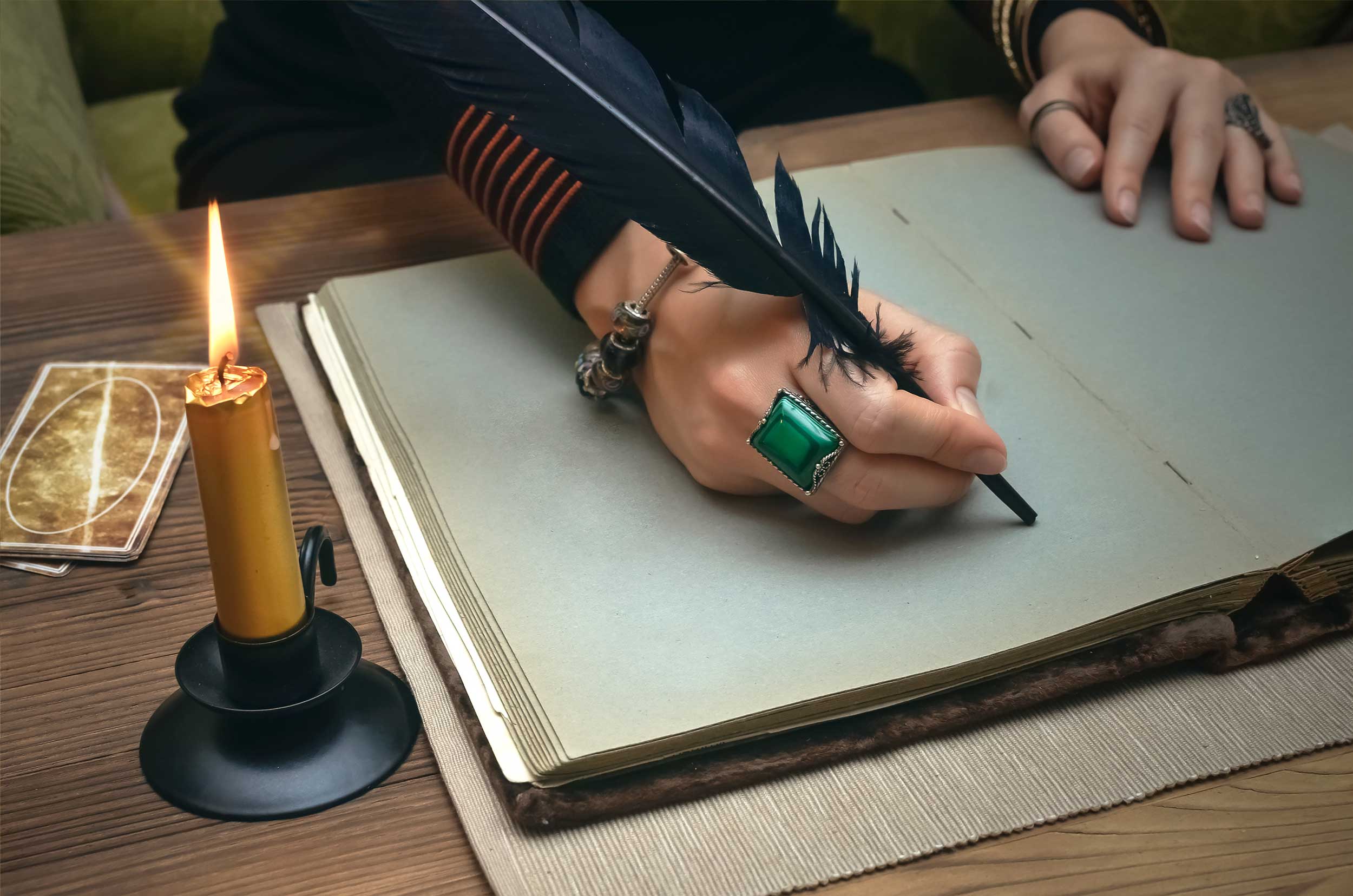 Hand holding quill pen, candle and tarot cards